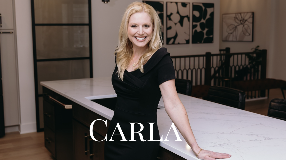 A smiling woman, Realtor, Carla Niziolek, in a black dress standing by a kitchen island with the text CARLA, She is the Best Realtor in West Michigan.